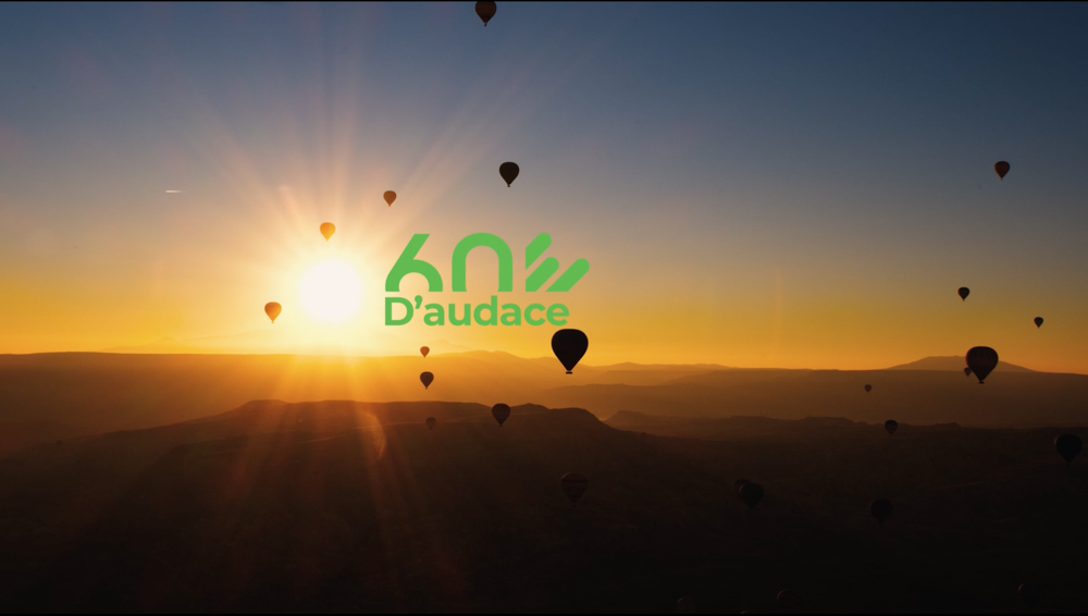 Des montgolfières au coucher de soleil avec le logo '60 ans d'audace' en vert superposé au centre de l'image.