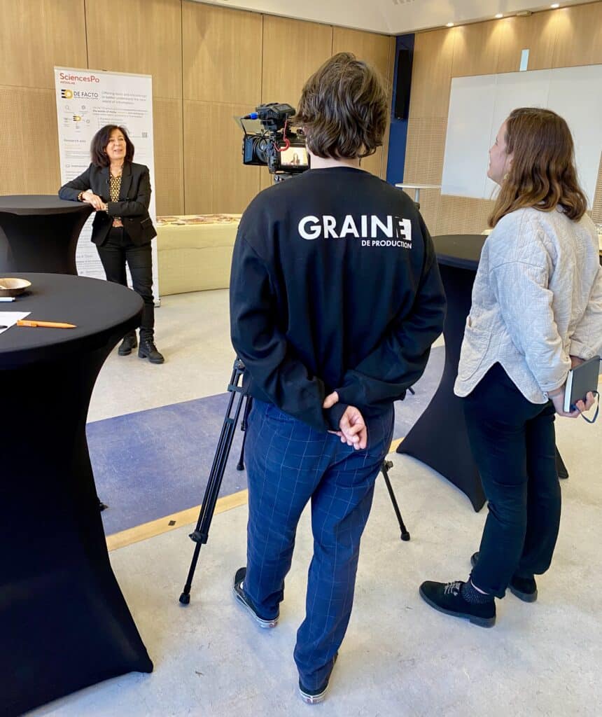 Une équipe de tournage en pleine interview d'une femme, avec une caméra et un micro, dans une salle de conférence à SciencesPo. Une personne de l'équipe porte un sweat noir avec l'inscription 'GRAINE de production'.