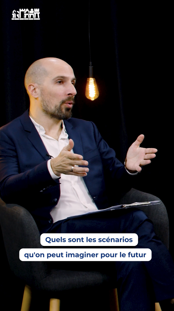 L'image montre un homme en costume assis sur une chaise, apparemment en train de discuter ou de donner une interview. Le texte en bas de l'image pose une question : "Quels sont les scénarios qu'on peut imaginer pour le futur". Cela suggère que la conversation pourrait être centrée sur des prévisions ou des spéculations sur les tendances à venir dans divers domaines, tels que la technologie, l'économie, ou les changements sociaux.